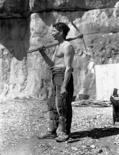 Old Bare-chested worker with a pick on his shoulder in a cave. The photograph was commissioned by the ILVA factory of Genoa